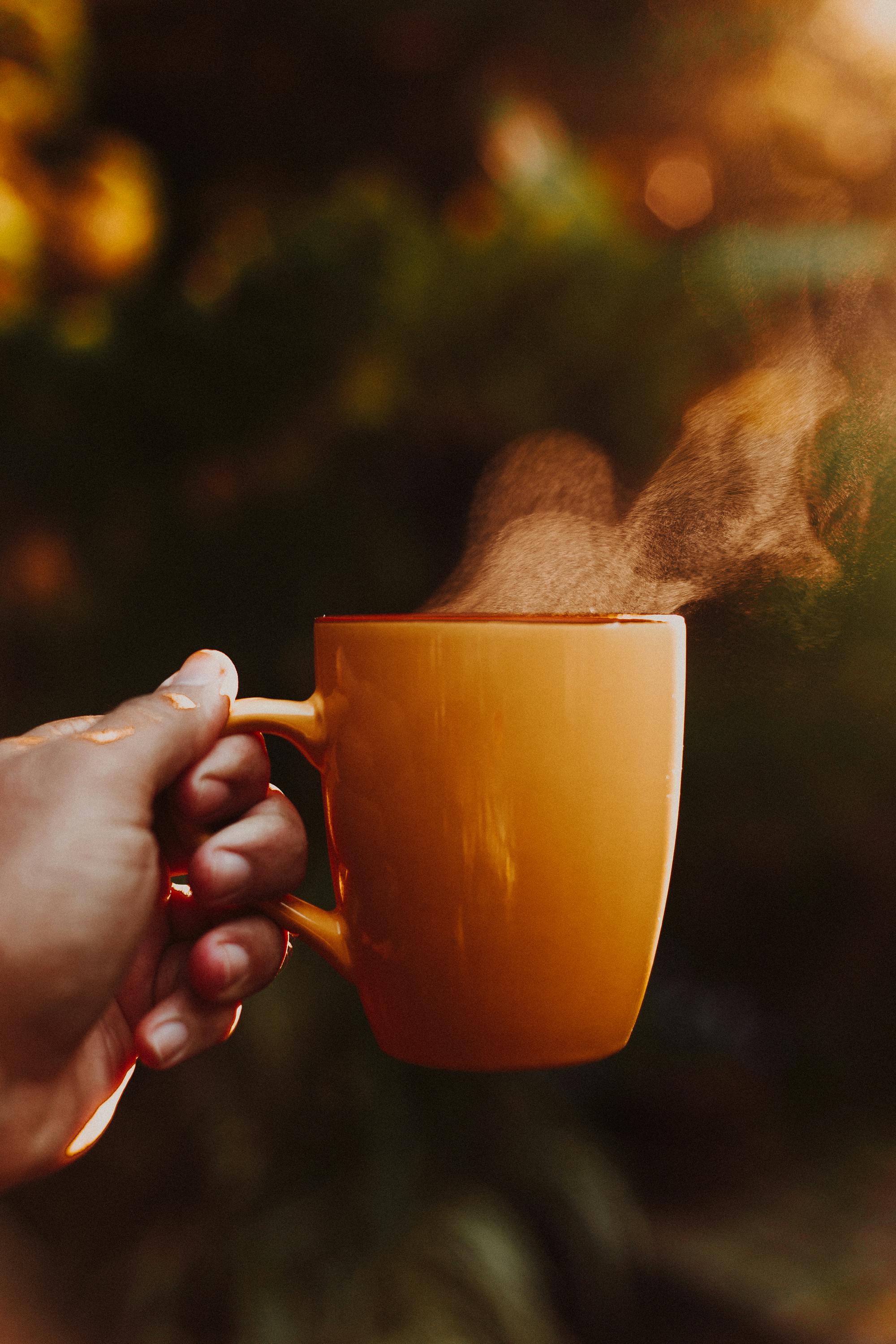 Mano izquierda sosteniendo una taza naranja con bebida caliente