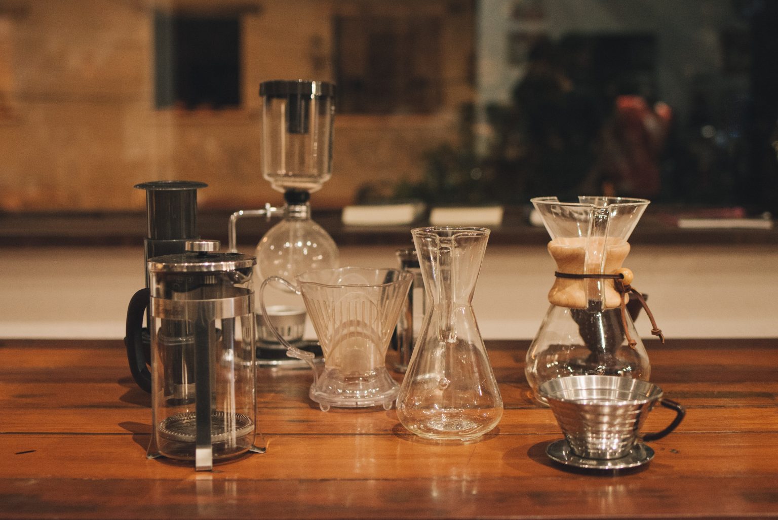 Mesa de madera con diferentes métos de preparación de café (prensa. sifón, Chemex, etc.)